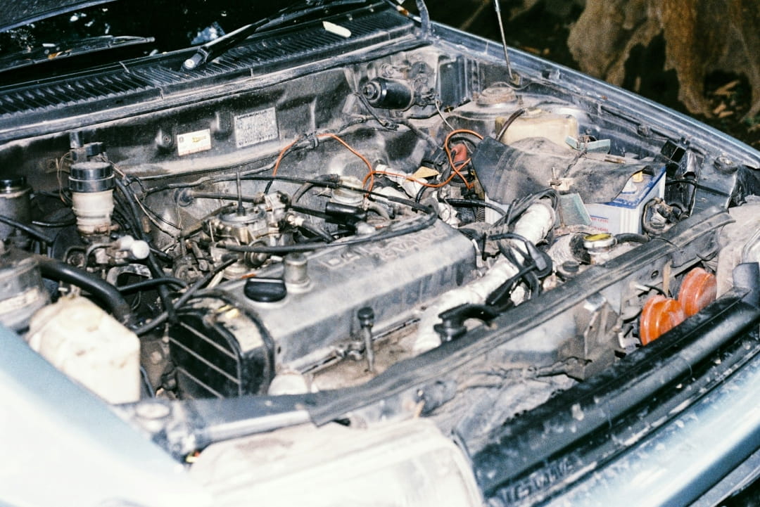 car engine bay with visible wiring, fuel components, and signs of wear or potential fire damage