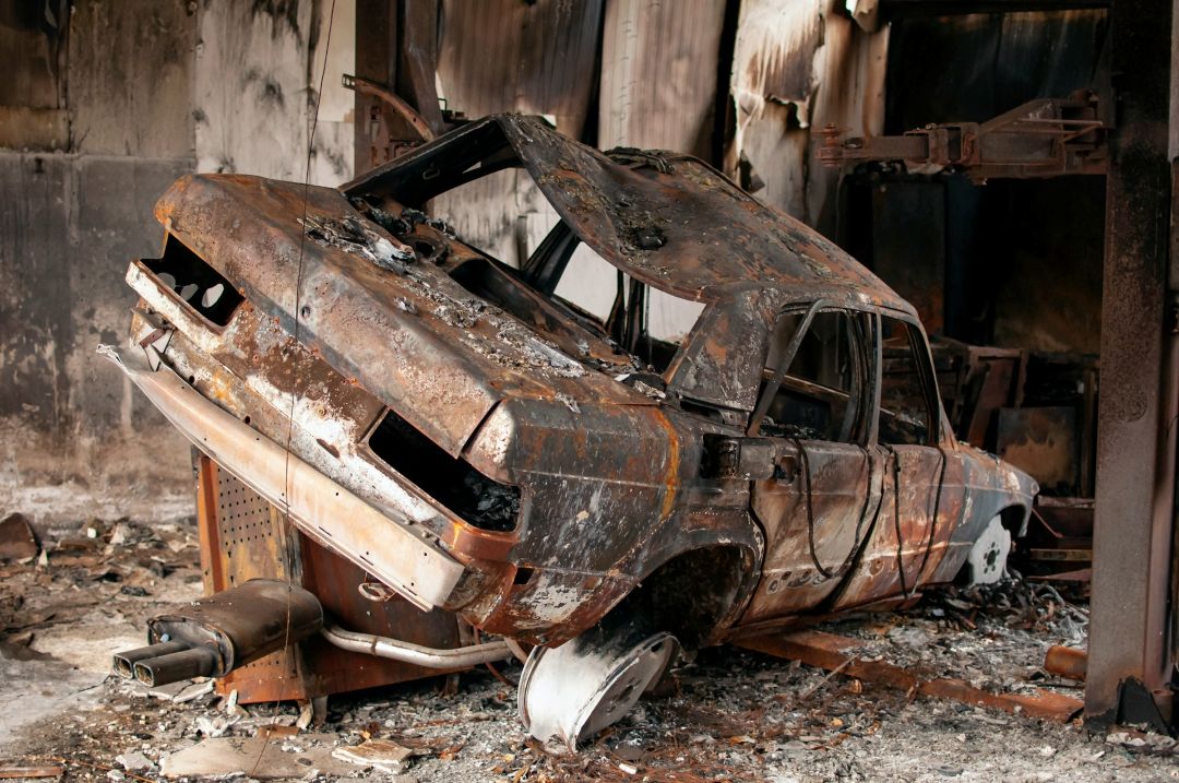 completely burned-out car with severe fire damage inside a destroyed structure