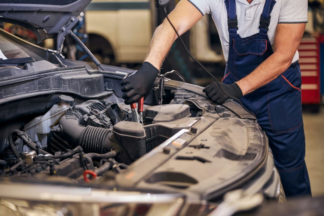 mechanic in overalls working under the hood of a car during a rebuilt title inspection