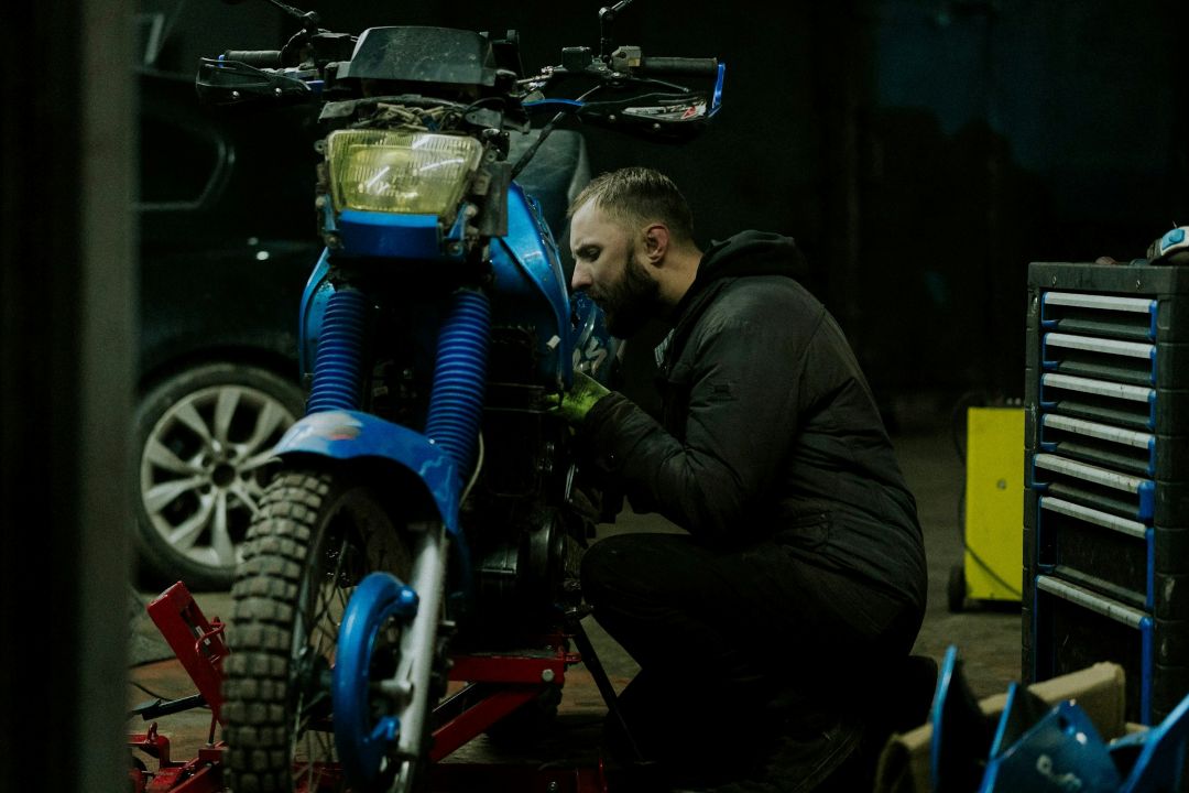 mechanic inspecting and repairing a blue motorcycle in a workshop