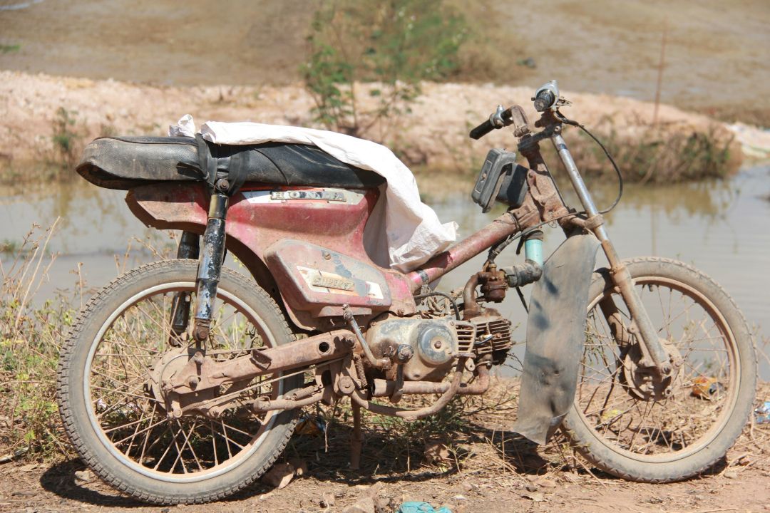 old rusted Honda motorcycle parked beside a small body of water, showing heavy corrosion